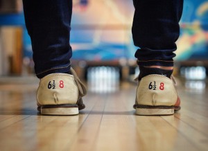 Persons feet shown standing on bowling alley, wearing rental shoes.